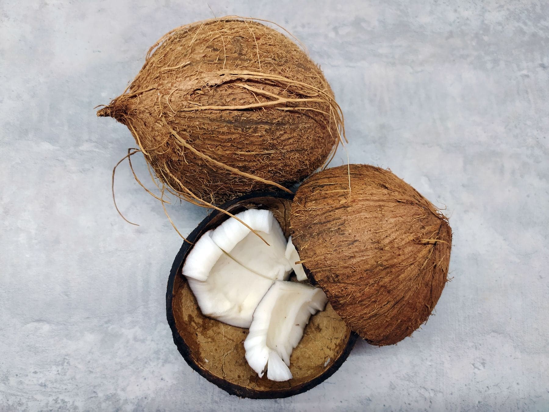 Two whole coconuts and one cracked open, showing pieces of white flesh