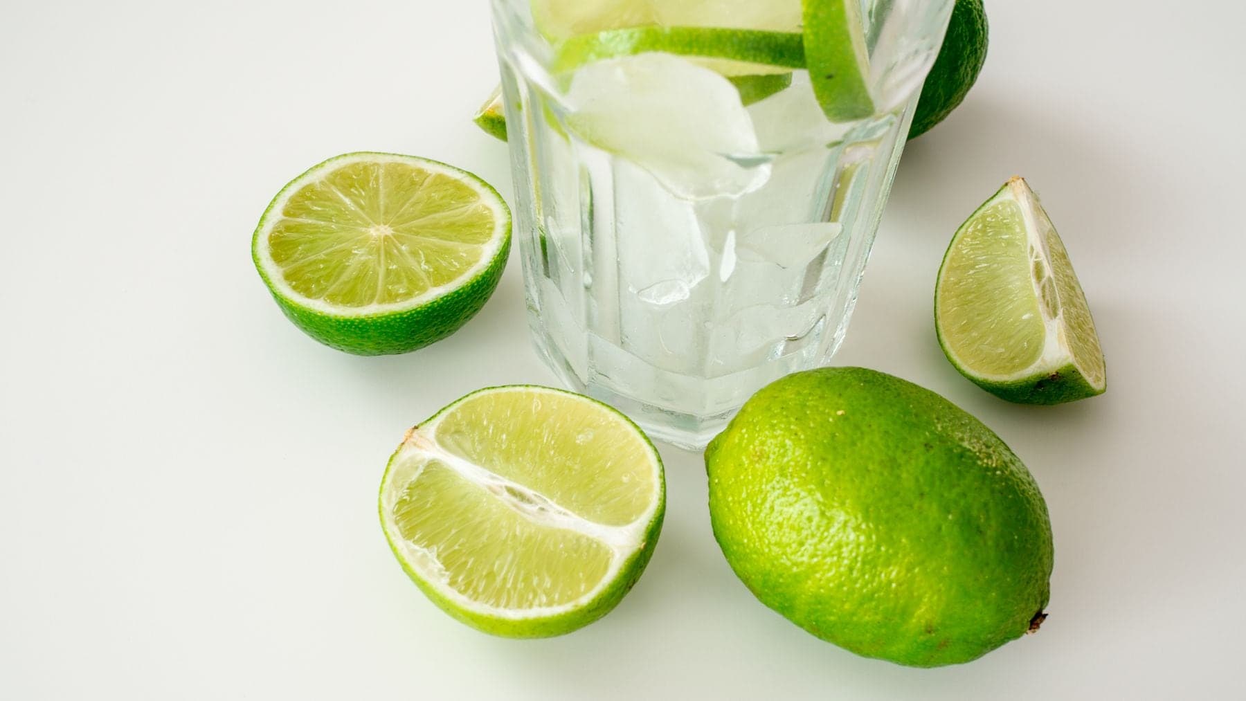A whole lime with lime halves and wedges on a white counter