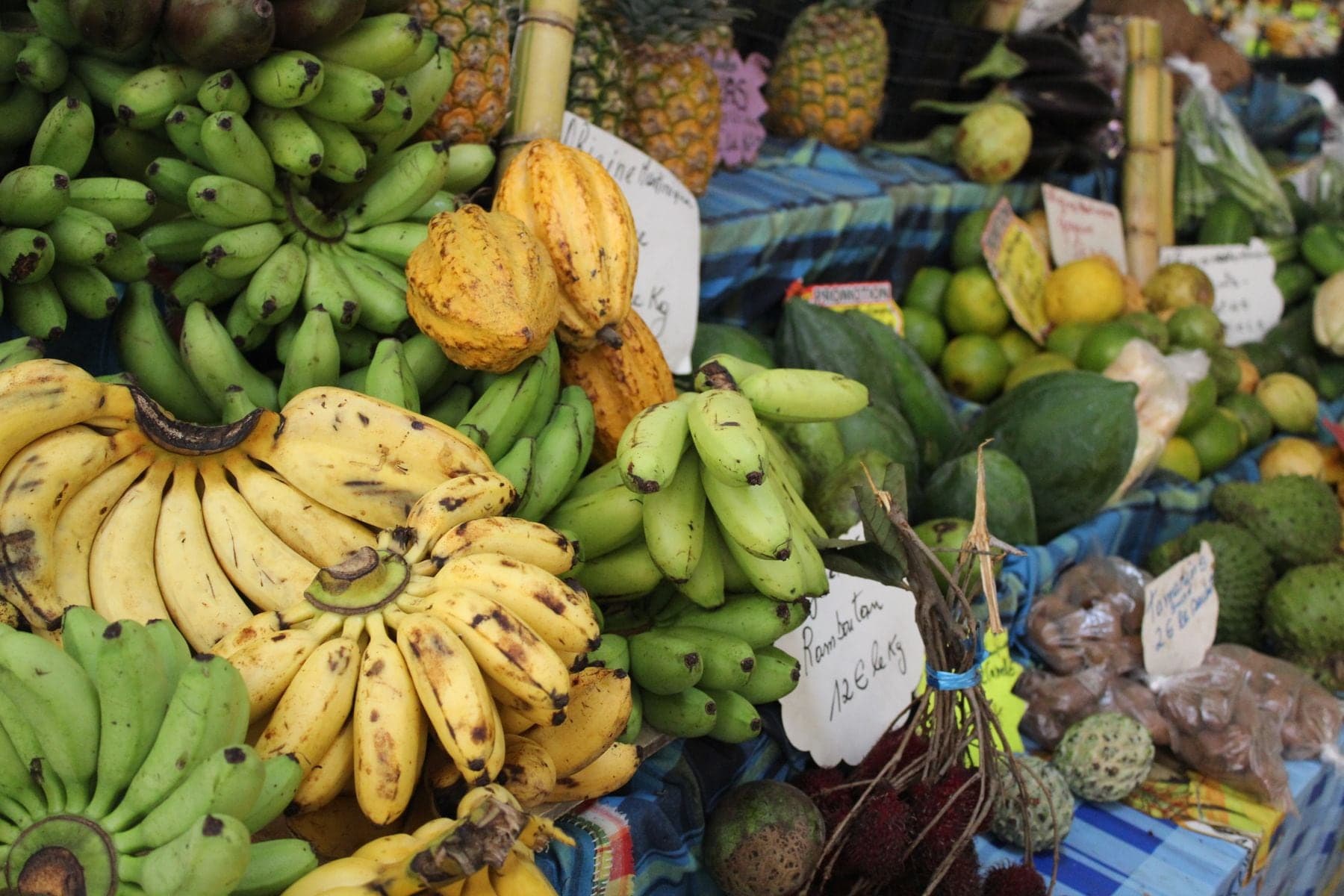 A market stall piled with bananas, cocoa pods, pineapples and limes