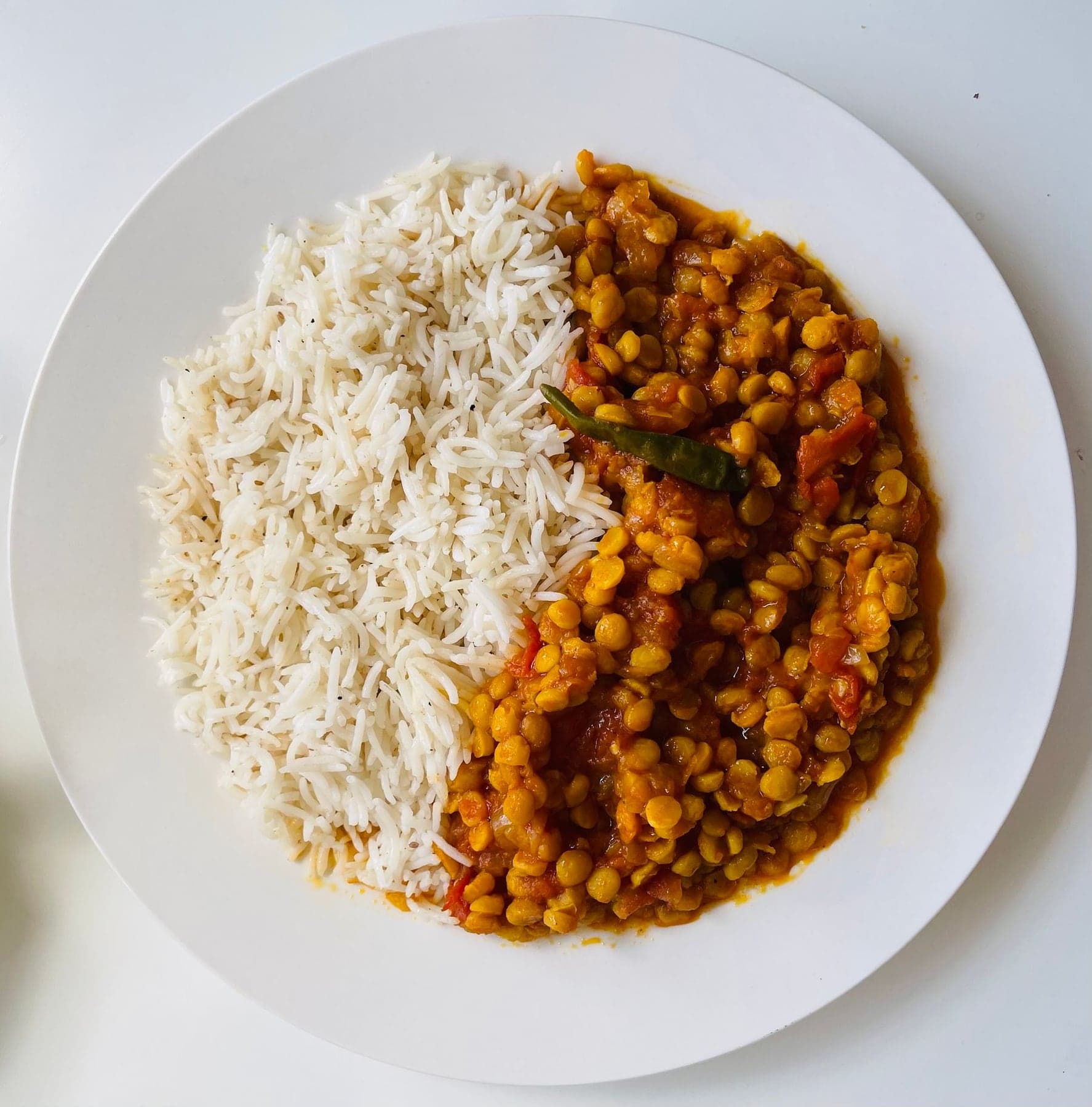 A white plate, half steamed rice and half curried chickpeas