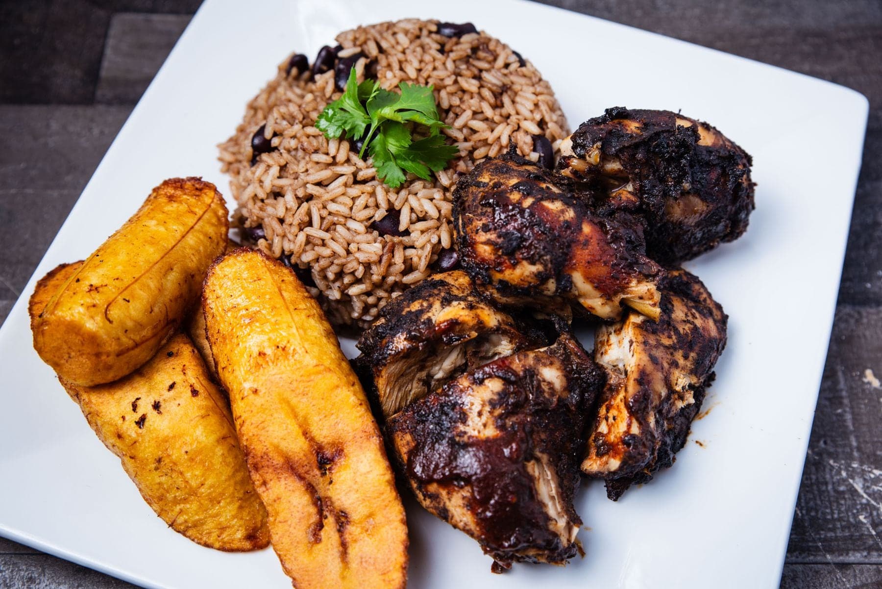 Jerk chicken with rice and peas and fried plantain on a white plate